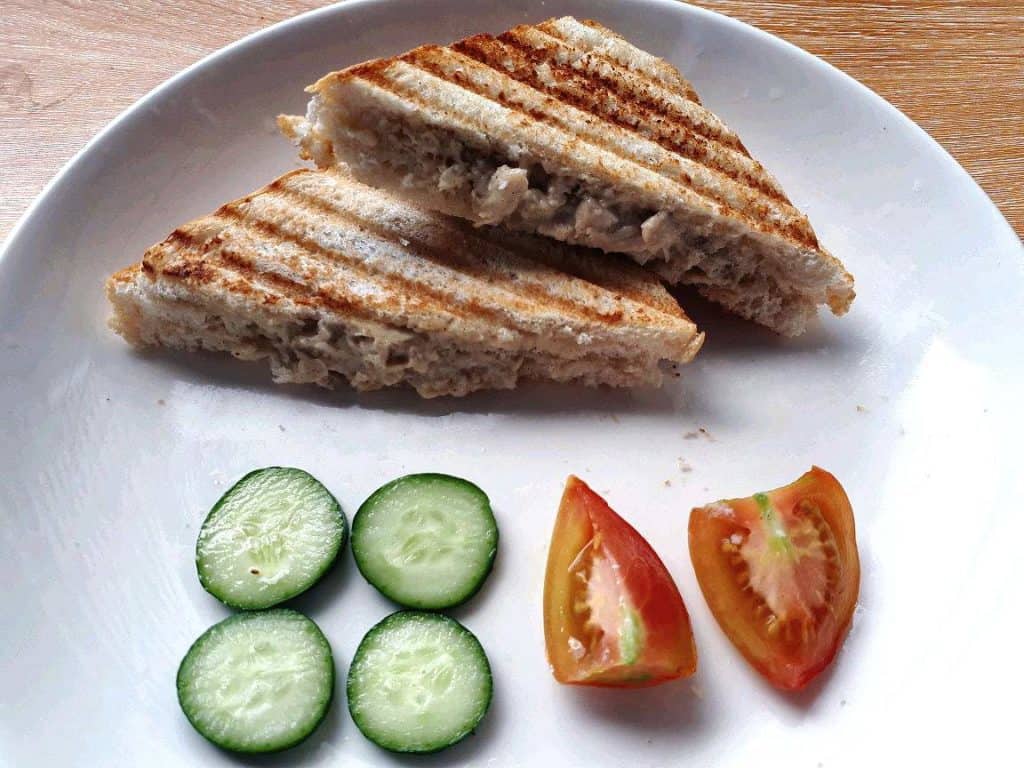 A Filipino style chicken sandwich spread  that is sliced into two served with slices of cucumber and tomatoes