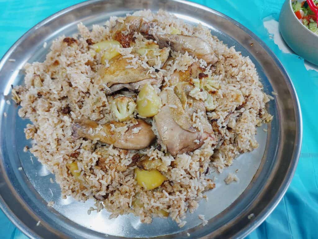 Chicken Maqluba with drumstick. thigh, cauliflower, eggplant, potatoes and rice served on a large round plate.