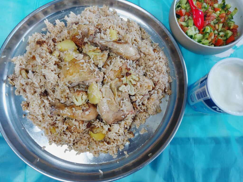 Chicken Maqluba with drumstick. thigh, cauliflower, eggplant, potatoes and rice served on a large round plate served with Arabic salad and plain yogurt.