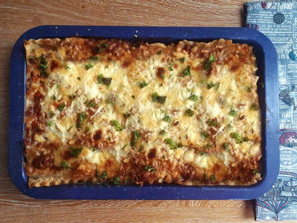 A Pinoy Lasagna Recipe topped with mozzarella and cheddar cheese and garnish with parsley in a pan.