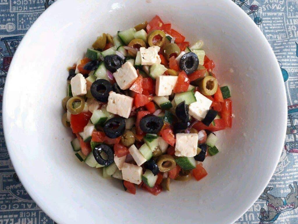 A Shepherd Salad Recipe mix with feta cheese, olives, tomatoes, and cucumber in a large bowl