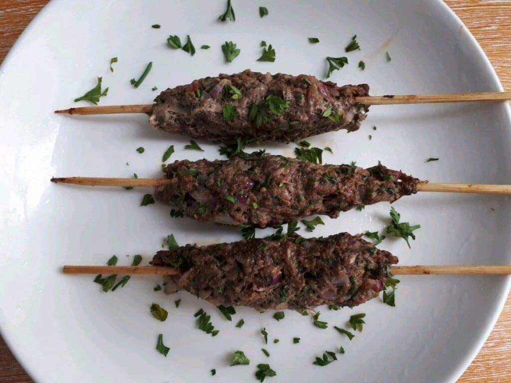 Beef Kofta Kebab serve in a wooden skewer and garnished with chopped parlsey in a plate