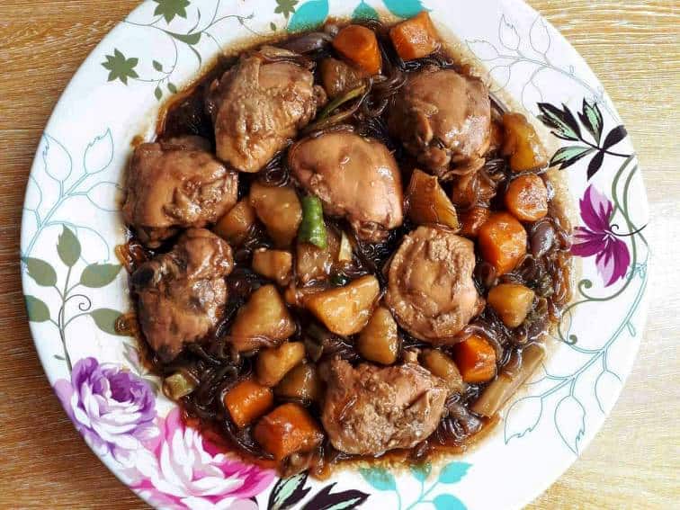  Recette d'Andong Jjimdak (poulet braisé coréen) servir avec des pommes de terre, des carottes, des nouilles en verre avec de la sauce soja et de la cuisse de poulet dans une grande assiette.