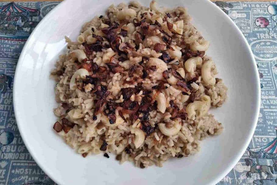 Egyptian Koshari Rice mixed with brown lentils, macaroni pasta and garnished with fried brown onion in a plate