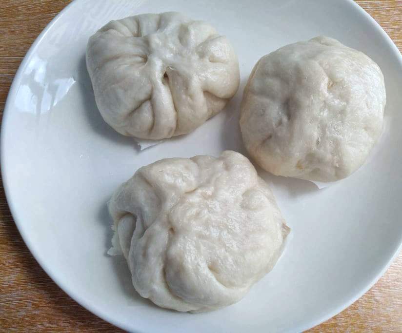 A white steamed bun filled with chicken siopao asado filling serve on a plate.