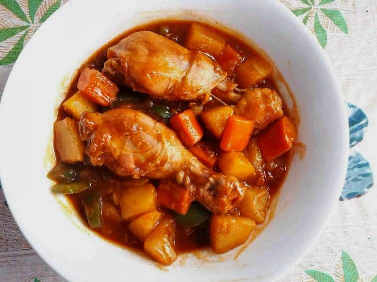 A Filipino chicken afritada recipe mixed with carrots, potatoes, green peas, bell pepper and tomato sauce in a plate bowl