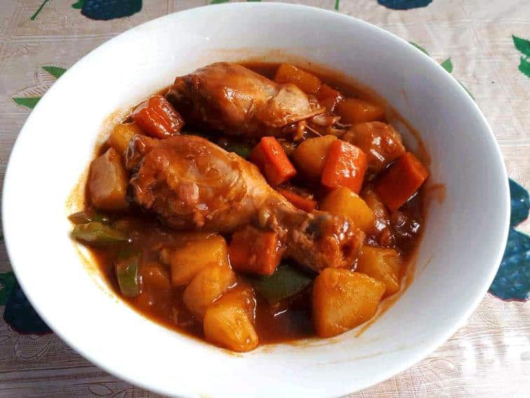 A Filipino chicken afritada recipe mixed with carrots, potatoes, green peas, bell pepper and tomato sauce in a plate bowl