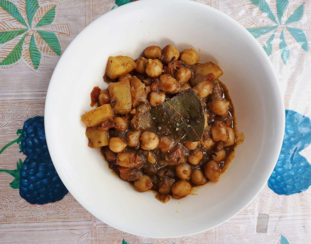 A potato and chickpeas curry recipe Aloo Chole with bay leaves, tomato sauces and other spices & herbs serve in a plate bowl