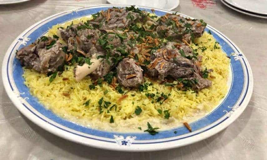 Jordanisches Mansaf, serviert mit Lamm und gelbem Reis, garniert mit frittierten Pinienkernen und gehackter Petersilie