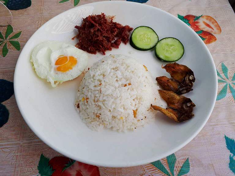 A filipino breakfast Cornsilog mixed with corned beef, garlic rice, sunny side up egg, sliced of cucumber and fried fish Danggit