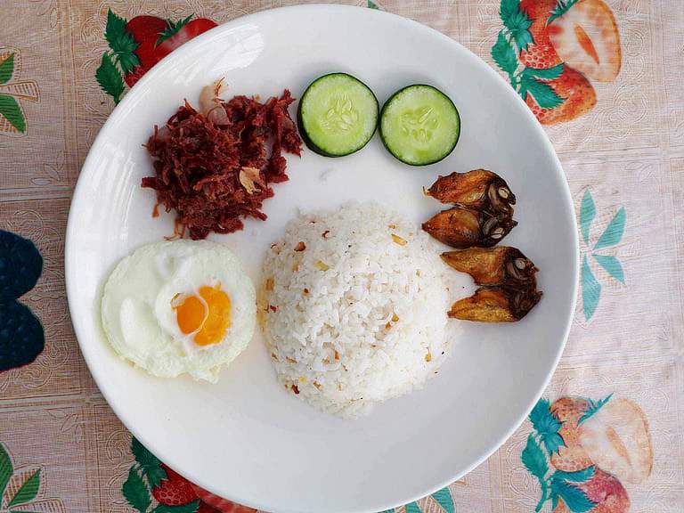 A filipino breakfast Cornsilog mixed with corned beef, garlic rice, sunny side up egg, sliced of cucumber and fried fish Danggit