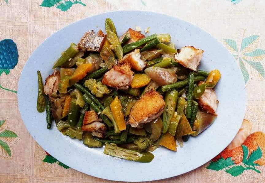 Pinakbet Ilocano recipe mixed with okra, bitter melon, eggplant, green beans and squash, chopped boneless fried fish on a plate
