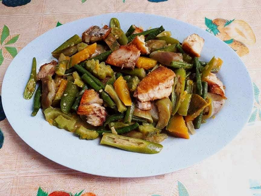 Pinakbet Ilocano opskrift blandet med okra, bitter melon, aubergine, grønne bønner og courgetter, hakket udbenet stegt fisk på en tallerken