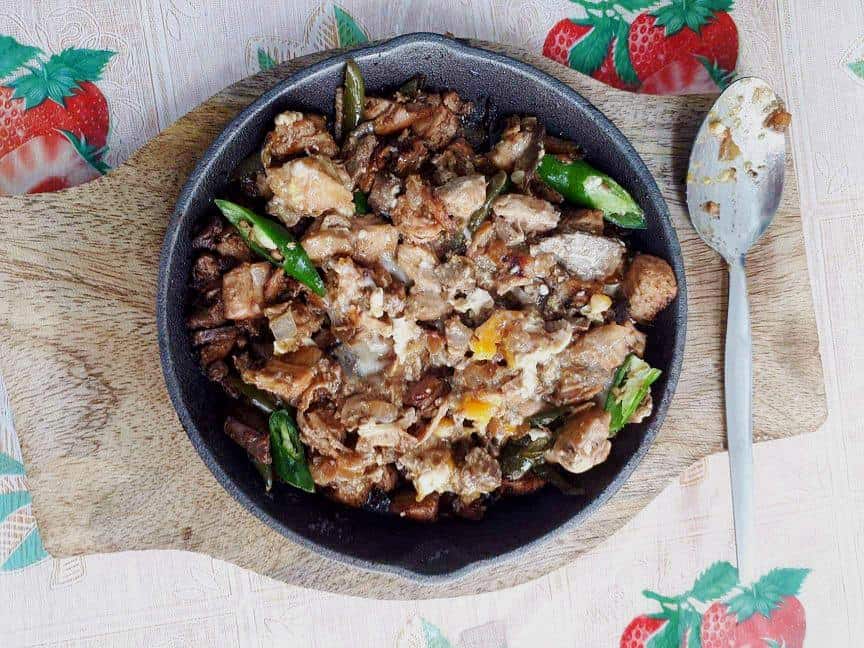 A filipino chicken sisig that is mixed with chicken liver & breast and green chilies serve in a caster iron plate.