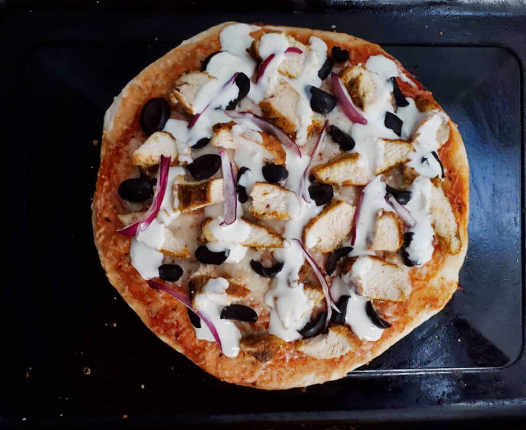 Chicken Shawarma Pizza Recipe with sliced chicken breast, black olives, red onion and drizzle with yogurt white sauce on a tray