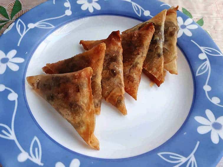 A triangular-shaped deep fried Indian pastry dish called Vegetable samosas serve on a plate