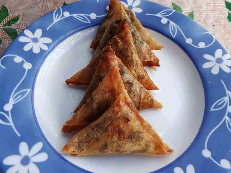 A triangular-shaped deep fried Indian pastry dish called Vegetable samosas serve on a plate