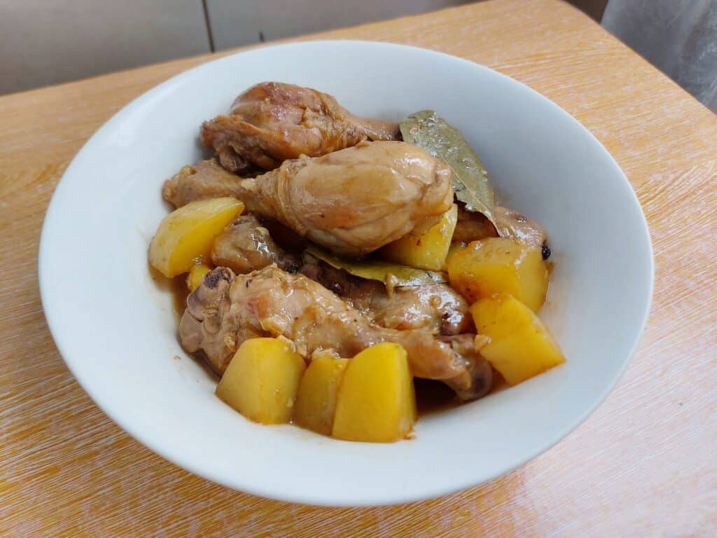 A filipino chicken adobo with potatoes, bay leaves, peppercorn served on a plate bowl