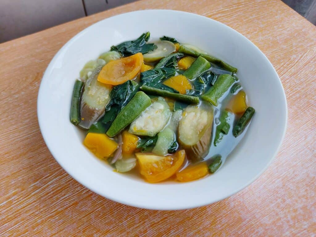 A filipino vegetable soup recipe Law Uy (Utan Bisaya) mixed with eggplant, patola, okra, tomatoes, green long beans, spinach leaves served in a plate bowl 