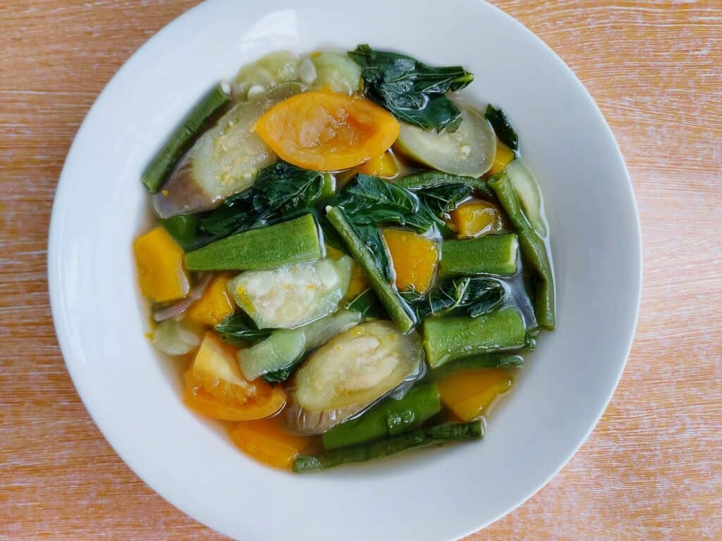 A filipino vegetable soup recipe Law Uy (Utan Bisaya) mixed with eggplant, patola, okra, tomatoes, green long beans, spinach leaves served in a plate bowl 