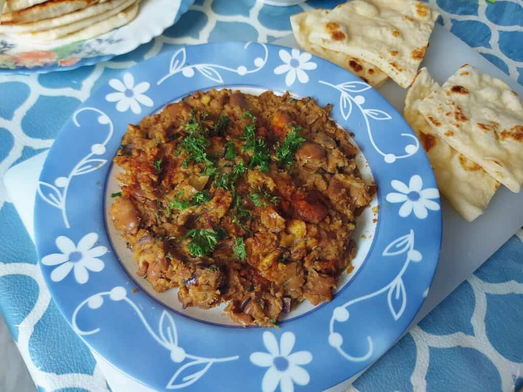 Egyptian Fava Bean Recipe Ful Medames that is topped with chopped parsley leaves and served with pita bread.