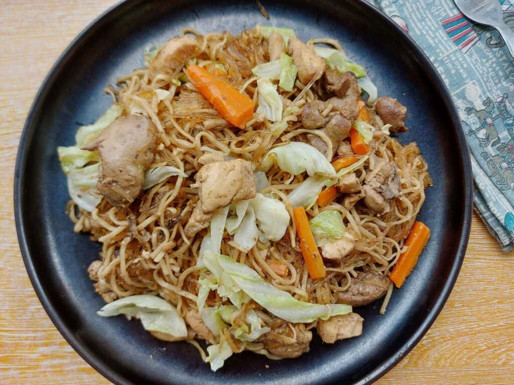 Filipino Pancit Bam-I recipe that is mixed with carrots, chicken breast and liver, cabbages and noodles served on a plate.