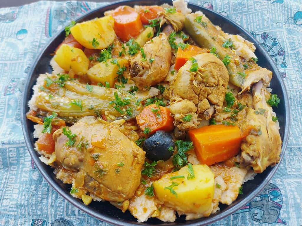 A Kuwaiti Gulf Arabic recipe Tashreeb that is mixed with chicken, potatoes, carrots and eggplant with pieces of flatbread under it and served on a plate.