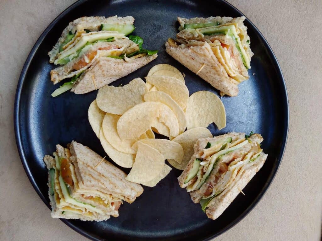 This is a Filipino clubhouse sandwich that contain ham, scrambled egg, lettuce, cucumber, tomatoes, cheese and mayonnaise  served with potato chips.
