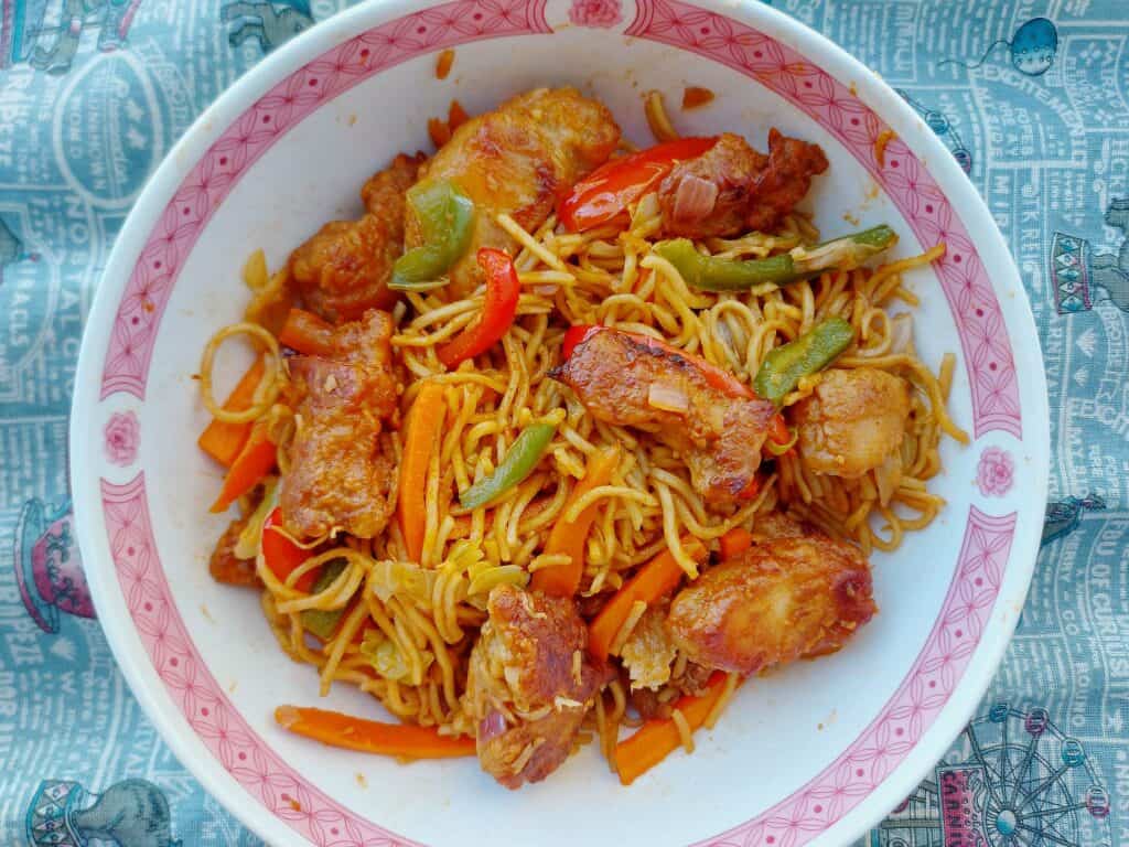 An indo-Chinese Chicken Manchurian noodle recipe mixed with fried boneless chicken breast, noodles,  julienned carrots and cabbages served on a plate