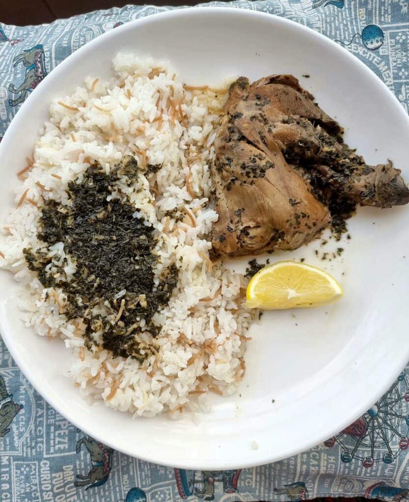 Middle Eastern green stew with chicken, molokhia leaves, garlic, herbs, and spices, served with rice or slices of lemon on a plate.