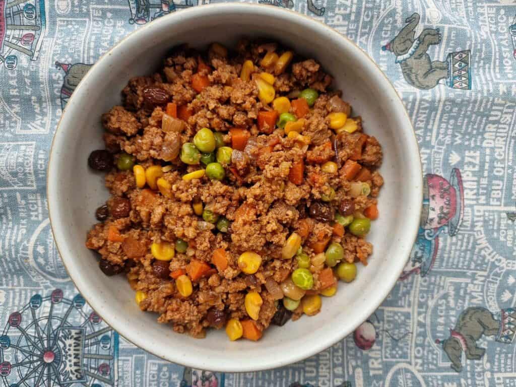 Filipino Beef Giniling mixed with ground beef, corn, carrots, green peas, raisins, and sauces served on a plate. 


