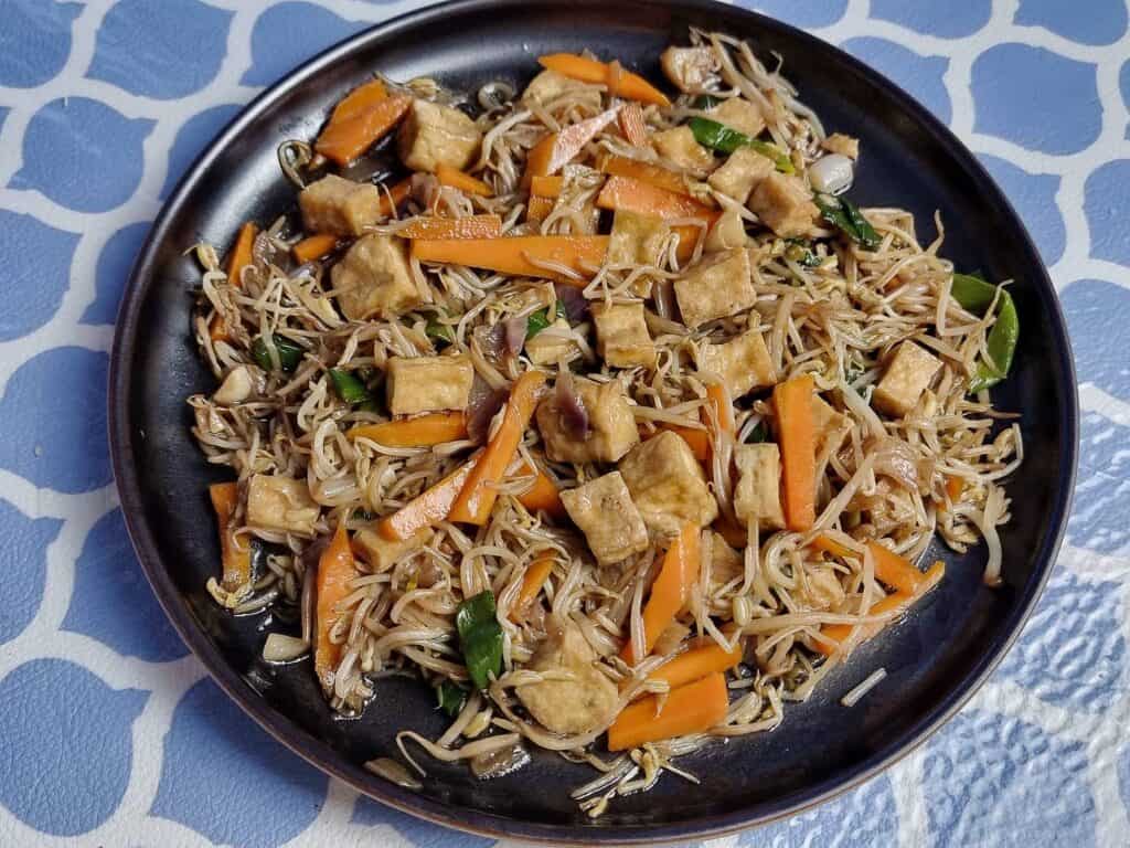 Filipino stir fried vegetable dish Ginisang Togue with Tofu, sliced carrots, bean sprouts, & green onion served on a plate. 
