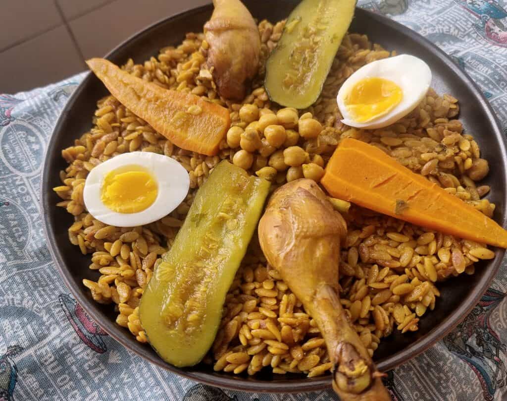 An Algerian Tlitli served with chicken drumstick, baton-cut zucchini, carrots, chickpeas in broth, served with layered boiled egg over orzo pasta. 