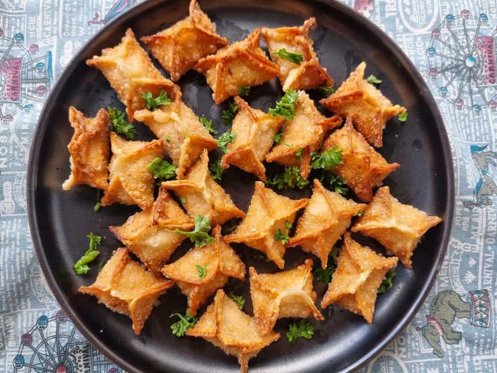 Golden-fried crispy buffalo chicken rangoons with creamy filling garnished with chopped parsley served in a plate.