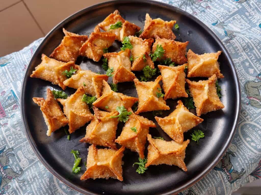 Golden-fried crispy buffalo chicken rangoons with creamy filling garnished with chopped parsley served in a plate.