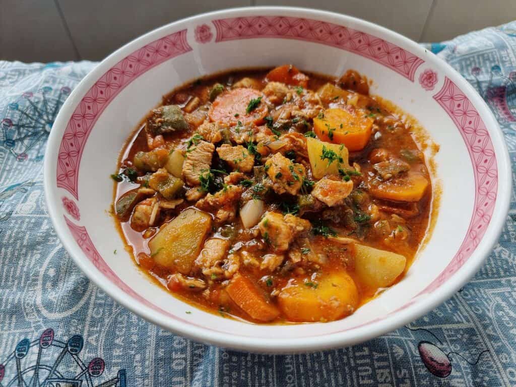 A turkish chicken stew Tavuk Sote that contain chopped boneless chicken breast with carrots and potatoes garnished with chopped parsley cooked in a tomato sauce served in a bowl.